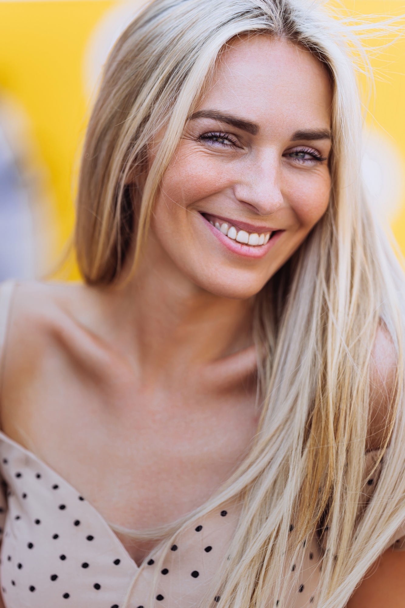 Vertical portrait of blonde Caucasian cheerful woman in beige dress toothy smiling looks at camera